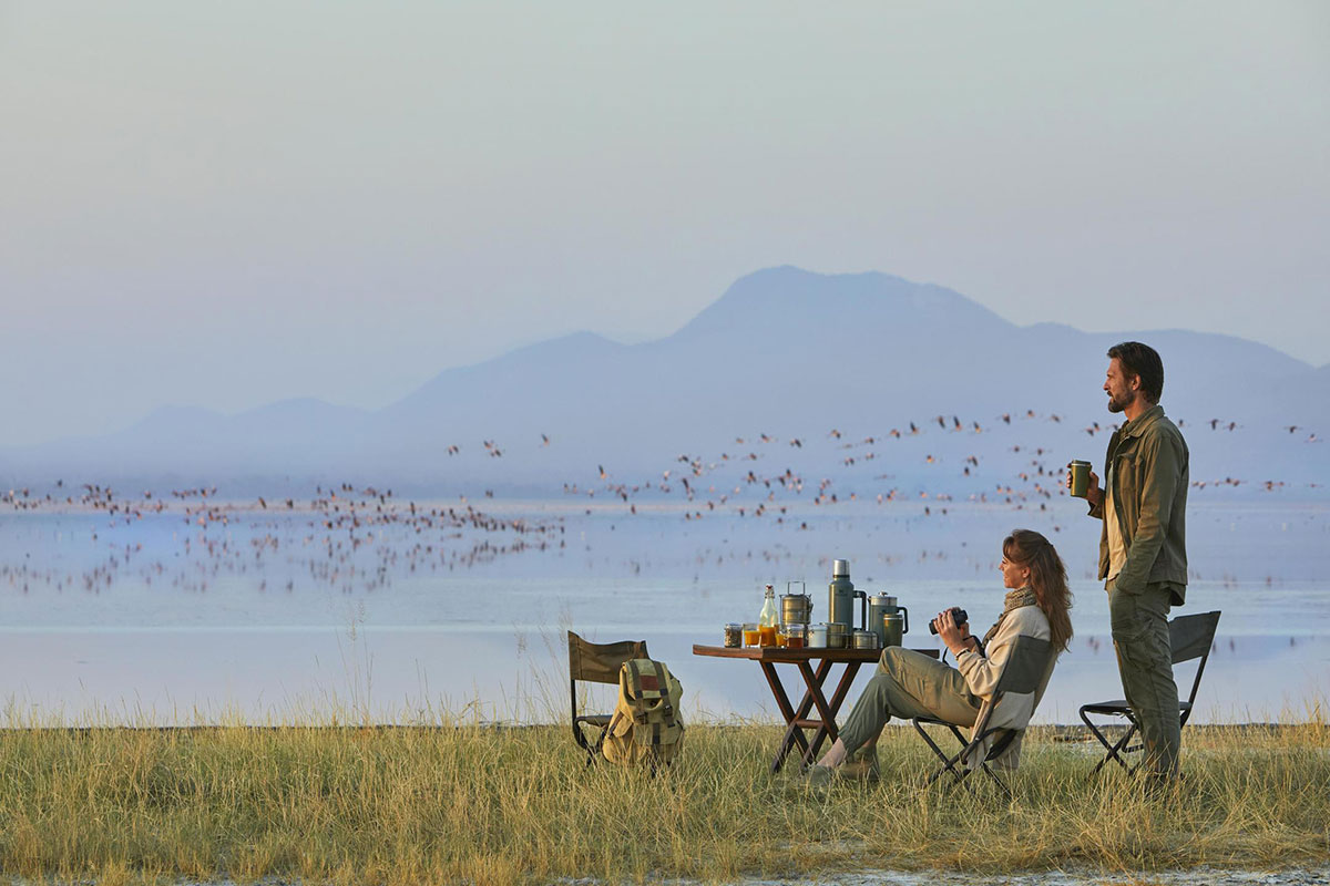 Man and woman drinking coffee while viewing wildlife, birds flying in the background